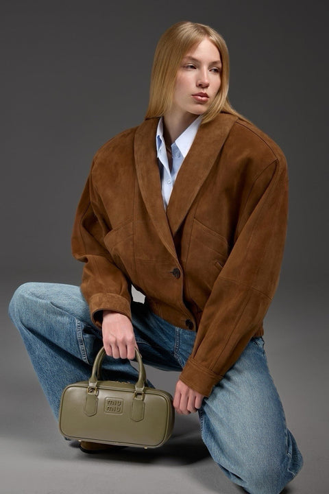 Stylishly dressed, a woman models a supple brown suede jacket featuring bold shoulders and a chic cropped silhouette.