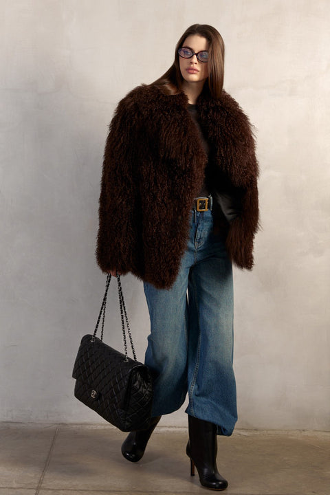 Draped in a luxurious brown Mongolian fur coat, a woman showcases the one-piece design with side slit pockets and a striking collar, lined with satin and leather for added sophistication.