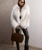 A woman wearing an oversized Crossed White Fox Fur coat, featuring voluminous natural white fur with silvery tones, offering a luxurious and luminous winter look.