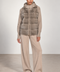 A model stands in a studio wearing a taupe faux-fur hooded puffer vest over a matching taupe knit hoodie and wide-leg knit pants, with taupe slip-on shoes.